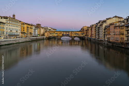 The iconic Ponte Vecchio bridge in Florence, Italy, illuminated at dusk with reflections shimmering on the Arno River