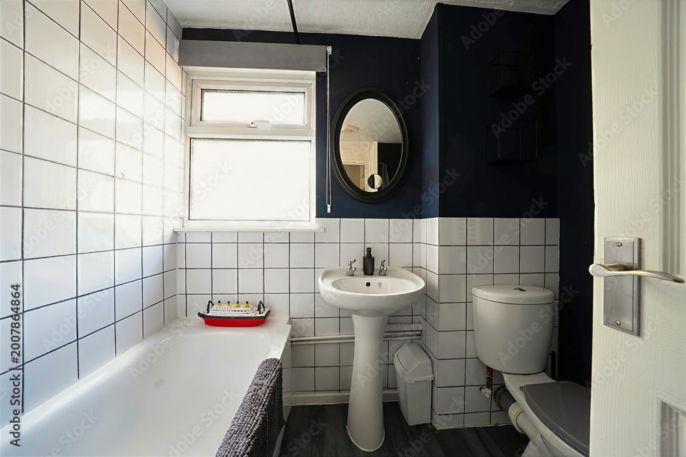 Fototapeta premium Interior view of a modern decorated bathroom with white tiled walls, a sink and toilet, plus an oval mirror and a bathtub