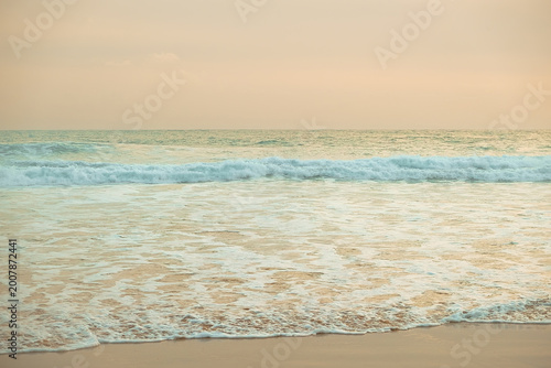 Foto Waves wash ashore on sandy beach during evening light near ocean