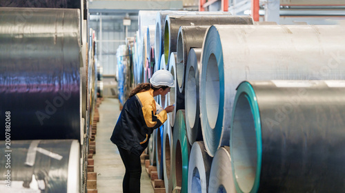 Bild auf Leinwand Caucasian man conducts detailed quality inspection of metal rolls with safety equipment and measuring tape in warehouse setting, assessing material specifications with focused expression