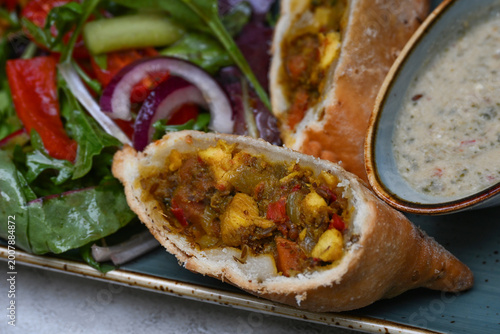 Samosa, traditional street food pastry from India or Persia, filled with chicken and vegetables, served with a hot dip and salad, selected focus