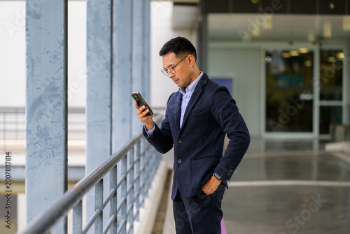 Asian businessman using smartphone, checking messages outdoors