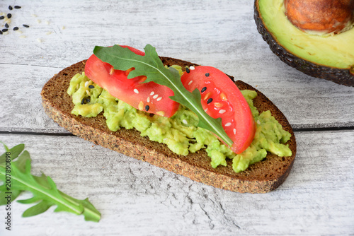 Foto smashed avocado toast with tomato and arugula on wooden background