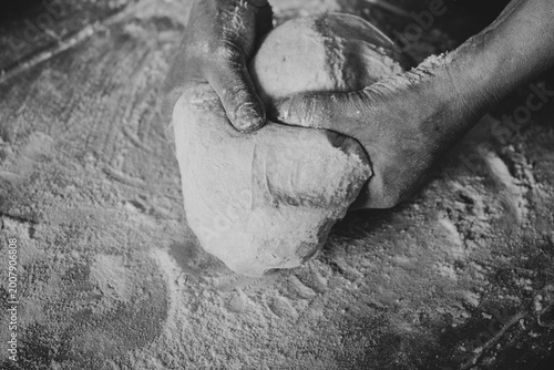 Skilled hands kneading artisanal dough with flour on the table, traditional gnocchi preparation, black and white photo.