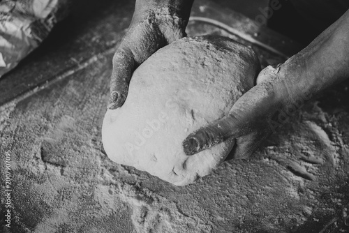 Skilled hands kneading artisanal dough with flour on the table, traditional gnocchi preparation, black and white photo.