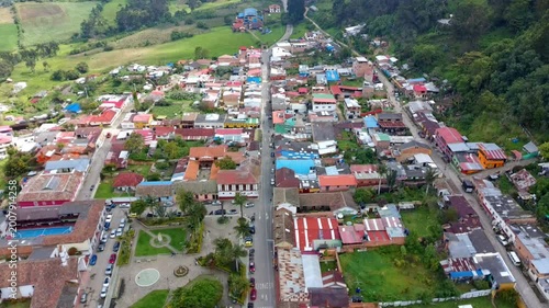 Aerial drone footage flying over the small town of Zipacon, Colombia. The view features the main street, a central park, colorful rooftops, and surrounding lush green mountains.