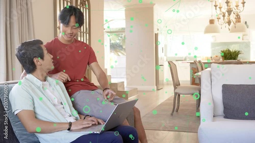 Teen typing laptop on sofa, father leaning over pointing, guiding learning, green overlay drifting