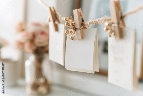 Rustic wedding decoration with blank cards hanging on a twine rope. Mockup for an invitation or place card holder with wooden clothespins. Celebration concept with gold decor