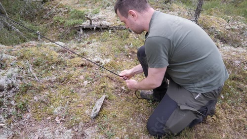 Man Securing Tent Guy Line with Stake in Forest Camping Setup