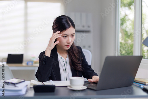 Billede på lærred Asian businesswoman working on laptop, experiencing stress or deep thought at he