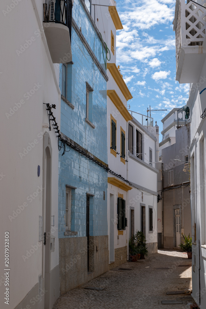 Fototapeta premium Narrow street in Olhao with traditional blue tiled building facade and white houses