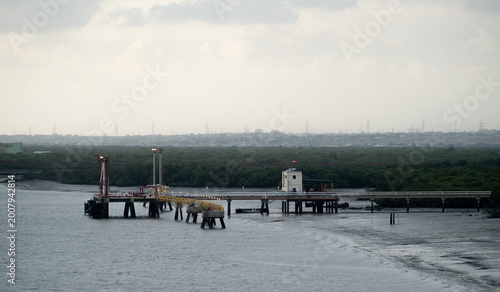 фотографія Industrial oil terminal pier extending across a mangrove shoreline beneath dramatic sun rays, illustrating coastal energy infrastructure, fuel logistics and maritime transportation
