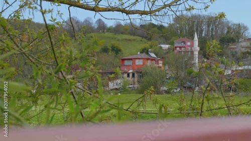 Rural Village with Mosque Minaret and Solar Water Heaters in Lush Green Valley in Spring