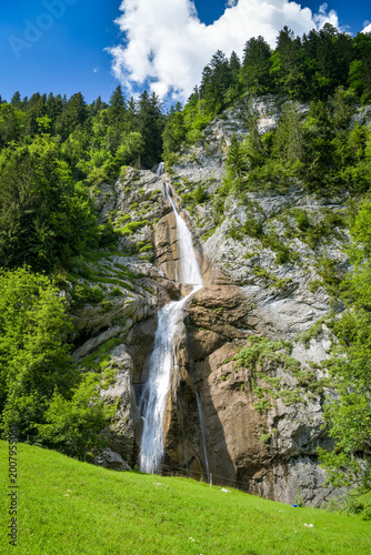 Waterfall on rocky cliff above green meadow