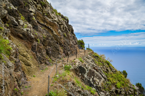 Narrow cliff path with rope railing above ocean