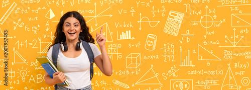 Fotografie A student stands against a bright yellow wall filled with math symbols and equations