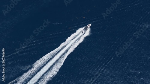 Aerial drone view of a sleek white luxury speedboat racing diagonally across deep navy blue ocean waters, leaving a long dramatic white foamy wake trail as a smaller blue boat enters frame.
