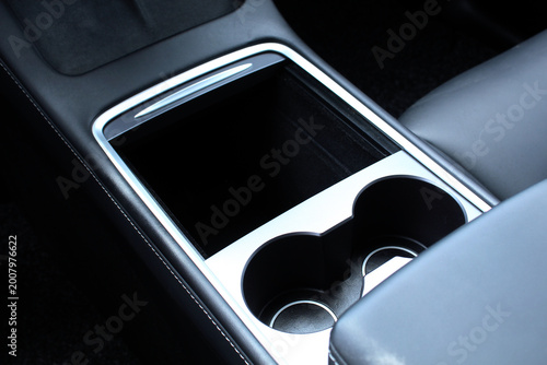 Sleek black automotive center console with spacious storage compartment, silver chrome trim accents, dual cup holders, and premium stitched leather materials. Armrest between front seats inside the ca