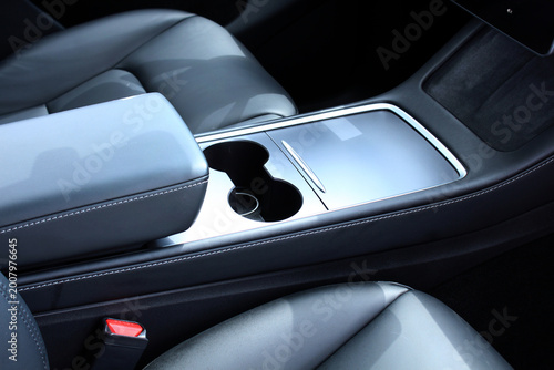 Armrest in the luxury passenger car between the front seats. Cup holders and armrest. Modern black leather automotive center console with dual cup holders, glossy storage compartment featuring silver 