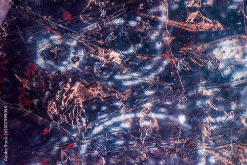 Glossy abstract texture shows scratched plastic, water droplets, reflections, and dark blue red light streaks. Blurred texture for overlay, background, backdrop, poster, banner, copy space