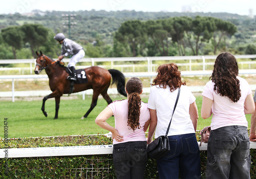 Foto Tres mujeres espectadoras en hipódromo viendo caballo de carreras apoyadas en va