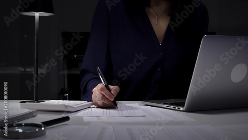 Businesswoman working late night typing on laptop at home office desk with documents and calculator. Audit and taxes in business