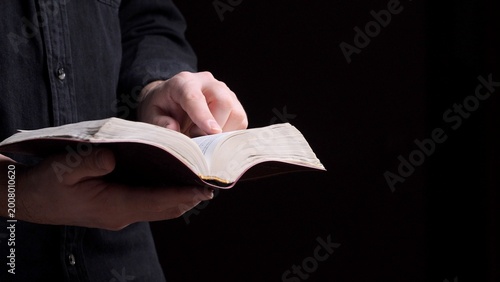 Konstfotografi Person's hands holding an open book, likely a bible, with a finger pointing at t