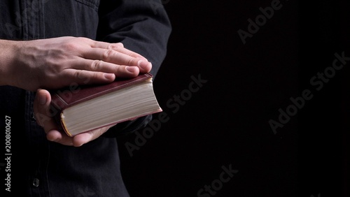 Obraz na płótnie Person's hands holding an old bible with one hand placed on top, illustrating co