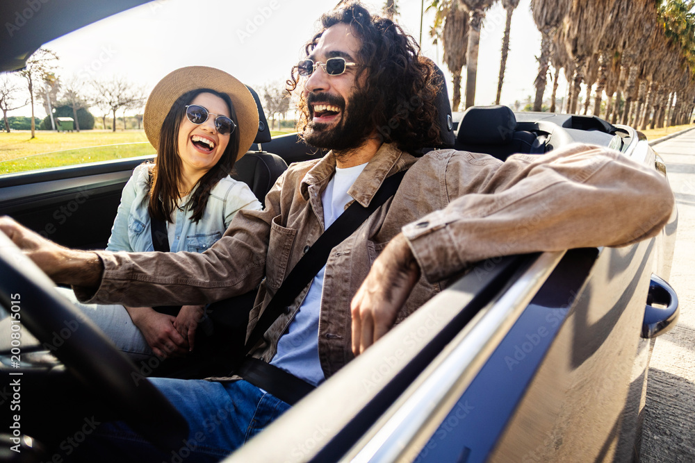 Obraz premium Young adult caucasian couple enjoying sunny convertible car ride. Relaxed man and woman traveling during summer vacation. Lifestyle and freedom concept.