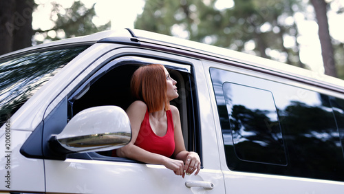 Woman with red hair looking out a white van window, enjoying the view during a spontaneous travel adventure