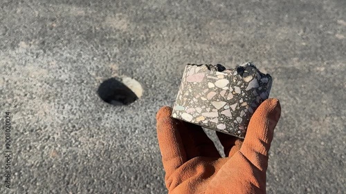 Worker holding asphalt core sample on road during inspection, 4K video
