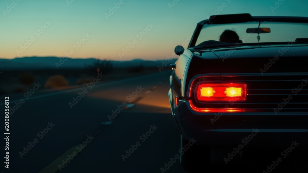 Naklejka premium Vintage convertible driving into the sunset on an empty highway.