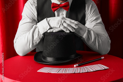 Photography Magician with hat and playing cards on table near red curtain