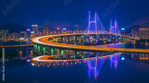 Brightly lit bridge at night with colorful reflections on water, urban cityscape photography.