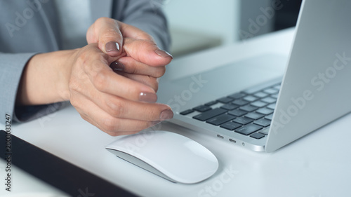 Trigger finger. Business woman painful thumb during working on laptop computer and mouse on table at office, occupational illness, office syndrome