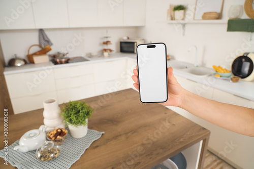 Woman with blank mobile phone in kitchen, closeup