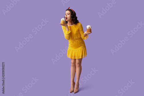 Beautiful pin-up woman eating Easter cakes on lilac background