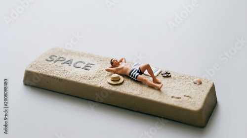 Miniature man sunbathing on a large keyboard spacebar representing leisure.