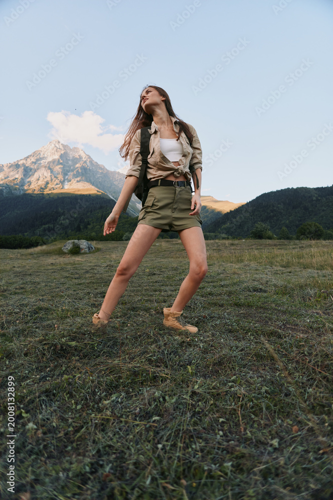Fototapeta premium Relaxed woman in a grassy meadow explores an outdoor landscape, wearing casual attire. Bright natural light, expansive sky, and distant mountains convey freedom, nature, and lifestyle.