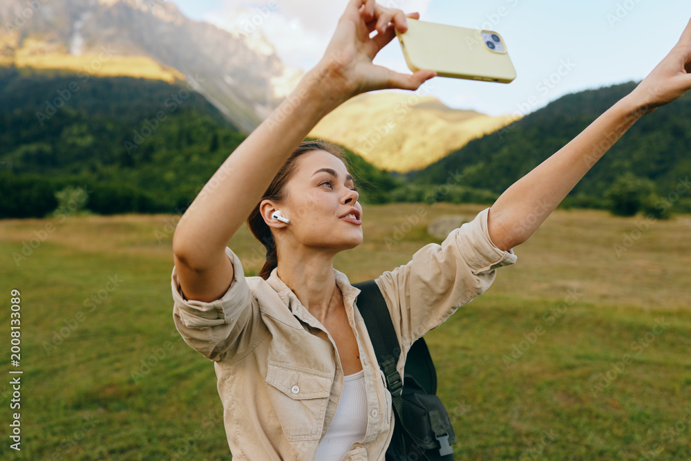 Fototapeta premium Bright outdoor moment with a woman lifestyle outdoors selfie in a mountain nature travel smiling casual portrait, sunlit backdrop and lush scenery