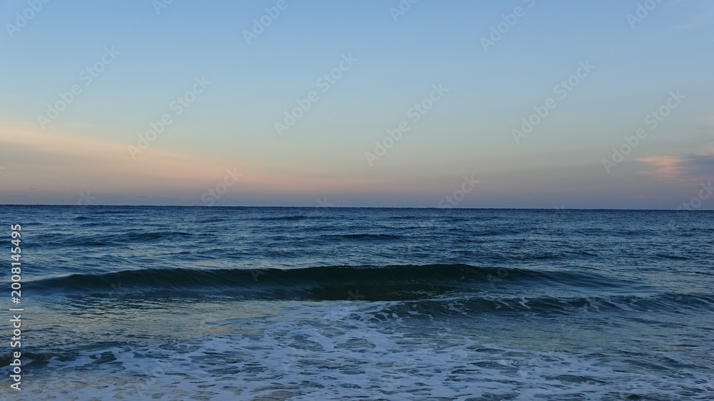 Fototapeta premium Peaceful Sea Waves at Dawn in Gangneung. Gentle white foam from waves washing ashore under a soft, pastel-colored morning sky. A serene and relaxing coastal scene at the East Sea.