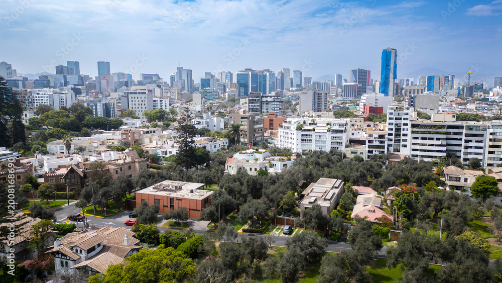 Obraz premium Vibrant panoramic view of San Isidro's financial district skyline viewed from the lush canopy of the historic El Olivar park in Lima, Peru.