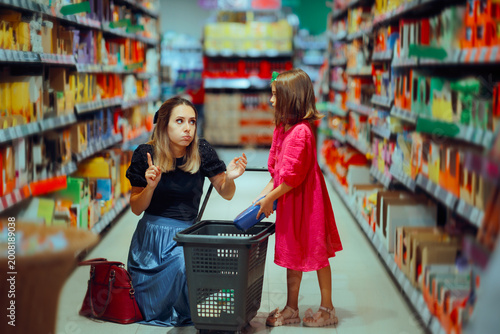 Mother Saying No to Child putting sweets in shopping basket. Mom gesturing no as her kid tries adding sugary snacks