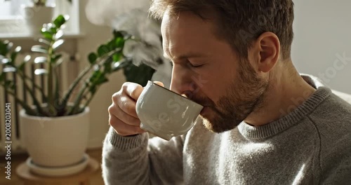 Man enjoying a steaming cup of coffee indoors, surrounded by plants and natural light