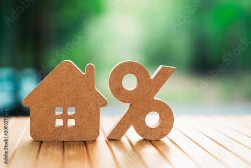 Real estate interest rate concept with wooden house model and percentage sign on wooden table. Mortgage, loan, property tax, and investment growth in housing market. Commercial stock image.
