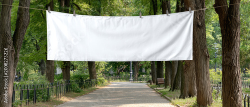 Blank white banner outdoor park walkway wire fence empty advertising sign horizontal cloth display urban nature background tree lined path scenery
