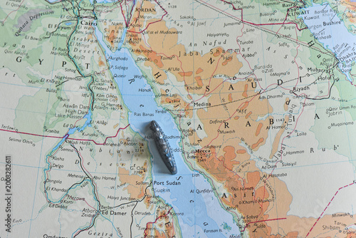 A small toy battleship placed on a vintage topographic map of the Red Sea, positioned between Egypt and Saudi Arabia, symbolizing maritime travel, shipping corridors, and naval strategy.