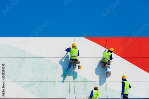 Workers paint a high building using a ladder, reflecting the risks of working at height, where safety, balance, and protective equipment are essential to prevent accidents.