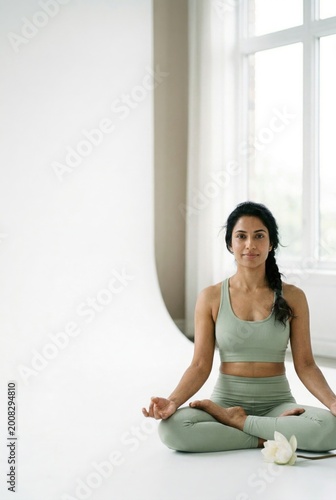 Free Download South Asian woman sitting in lotus pose on a white floor for wellness advertising, yoga studio mockup and holistic lifestyle branding with copy space for text - GFXLoad