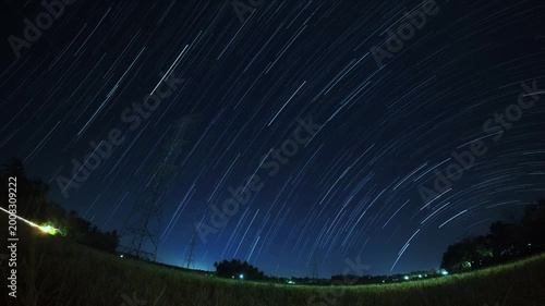 Nighttime landscape featuring star streaks moving across the deep blue horizon above a field.